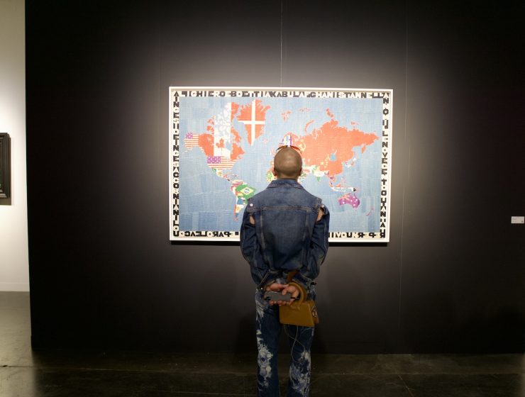 Tariffs and the global art market at Miami Art Week. Visitor views international artwork highlighting cross-border exchange at an art fair.